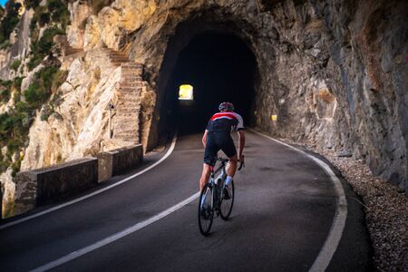 Man on road bicycle ride on the road in mountains.. Dark rocky tunnel on the Road. Sa Calobra, Majorca, Spainの写真素材