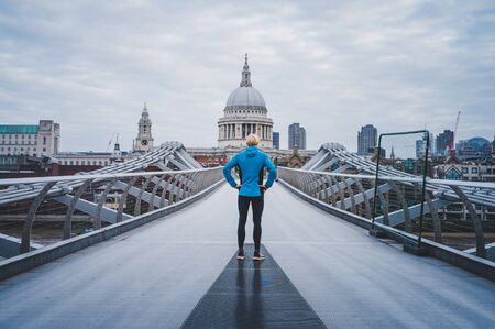 Young active man standing at Millennium Footbridge over the Thames and looking at St Paul's Cathedral..の写真素材