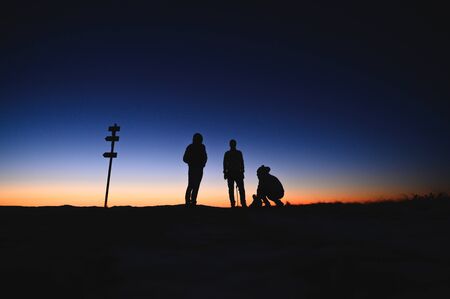 Three tourist standing on the ridge of morning mountains. Sunrise colors in backgroundの写真素材