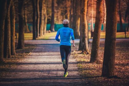 Runner in park, wear blue running functional clothes, train in alley of treeの写真素材
