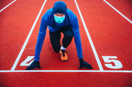 Runner wearing medical mask, Coronavirus pandemic Covid-19 in Europe. Sport, Active life in quarantine surgical sterilizing face mask protection. Outdoor run on athletics track in Corona Outbreakのeditorial素材