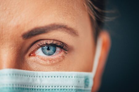 Close up portrait photo, Eye of Yong Female Doctor. Protection against contagious disease, coronavirus, hygienic face surgical medical mask to prevent infection. Black backgroundの写真素材