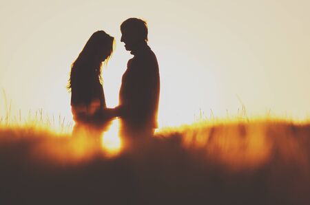Man and woman in love standing in rye field during colorful summer sunrise - vintage photo with copy spaceの写真素材