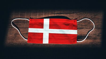 Denmark National Flag at medical, surgical, protection mask on black wooden background. Coronavirus Covidâ19, Prevent infection, illness or flu. State of Emergency, Lockdown...の写真素材