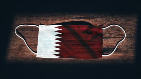 Qatar National Flag at medical, surgical, protection mask on black wooden background. Coronavirus Covidâ€“19, Prevent infection, illness or flu. State of Emergency, Lockdown...