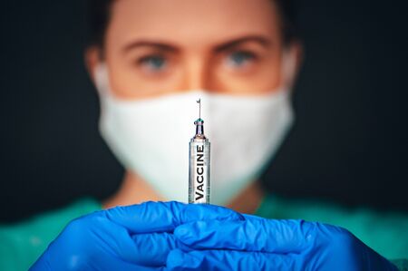 Coronavirus Covid-19 Protection and Vaccine. Female medical Scientist working on Vaccine from from, flu, coronavirus, ebola, TB. Protective suit and mask holds injection syringe and vaccine.の写真素材