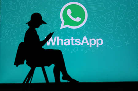 NEW YORK, USA, 25. MAY 2020: WhatsApp cross-platform messaging and Voice over service Young woman silhouette sitting on chair and playing on her smartphone. Company logo on screen in backgroundのeditorial素材