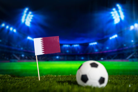 Qatar National Flag on Green Grass of illuminated Football Stadium at Nightの写真素材
