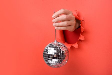 Hand holding Silver disco mirror ball on torn red paper wall. Copy space aside for your advertising...