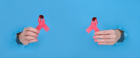 Red ribbon is symbol of fight against AIDS or disease cancer of female breast. Girls hand holds a...