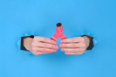 Red ribbon is symbol of fight against AIDS or disease cancer of female breast. Girls hand holds a...