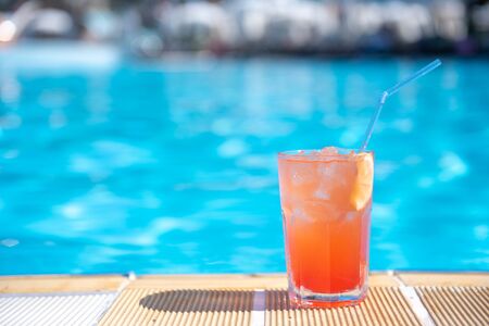 Fresh alcoholic red cocktail sex on beach with ice in glass on edge of pool in summer weather...