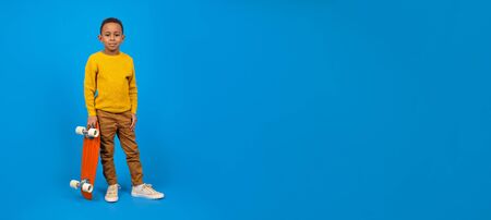 Cute African-American teenager in casual clothes, yellow sweater and brown pants, standing and...
