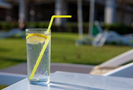 Cocktail with lemon in a glass on the beach of the sea on the background of sun loungers for relaxation. The concept of rest and relaxation, a place for the testの写真素材