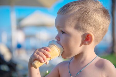Child has ice cream in a waffle cup against the backdrop of a summer beach with palm trees, sea and loungers for relaxationの写真素材
