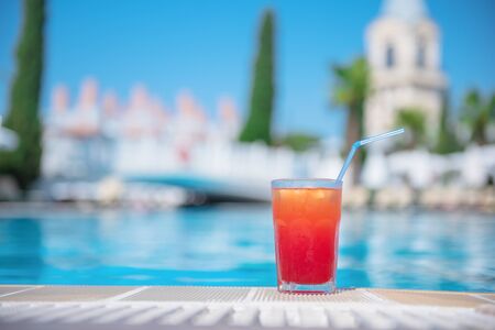 Fresh alcoholic red cocktail sex on beach with ice in glass on edge of pool in summer weather...