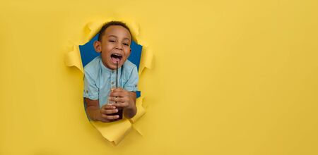 Happy cheerfully smiling African-American boy holds bottle of juice, drinks red cherry drink from...