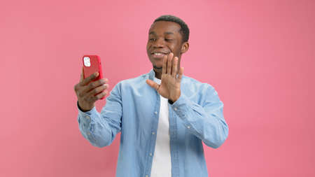 Cute smiling black man, African American 20 years old in denim shirt, answers video phone call,...