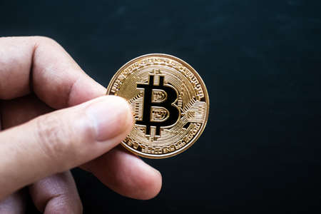 The hand holds a gold bitcoin coinの写真素材