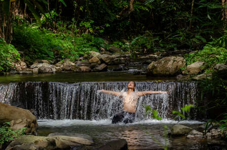 Asian man relaxing with freedom open arms in waterfall in tropical nature. Wellness spa concept in holiday nature.の写真素材