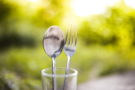 Fork and spoon in empty glass on wood table with sunlight and green backgroundの写真素材