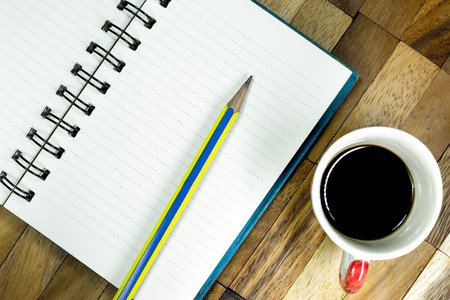 Notebook and pencil with black coffee on table,Desk office with working device,Blank notebook on wood in work officeの写真素材