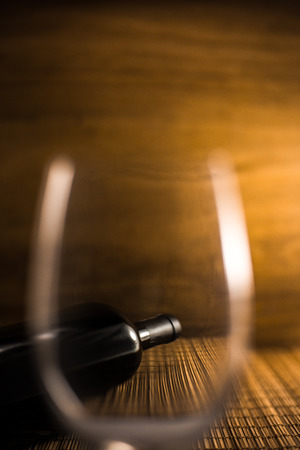 empty glass and alcohol bottle on wooden,Photograph a bottle of wine through an empty glassの写真素材