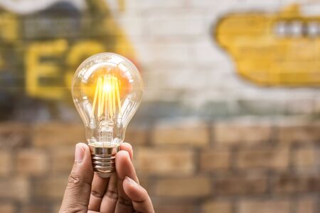 A hand is holding a light bulb with art wall. Object symbol for save energy conceptの写真素材
