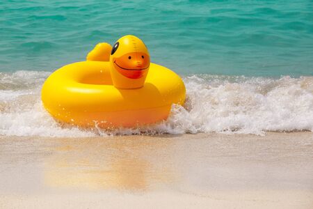 Inflatable ring player with soft wave of blue ocean on sandy beach. Background of travel in summer seasonの写真素材