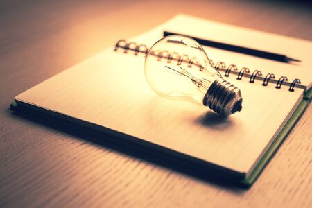 Blank notebook and pencil with light bulb on wooden table.creative ideas of writer, thinking for...
