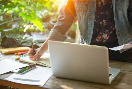 A business women is working on desk office with her computer laptop and writing accounts for...
