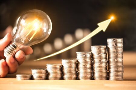 Saving money graph and hand holding a light bulb on coins. Background for business ideas and design....