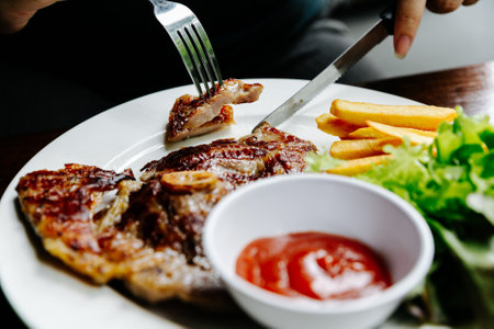 eating steak on white plate with fork and knife on his handsの写真素材