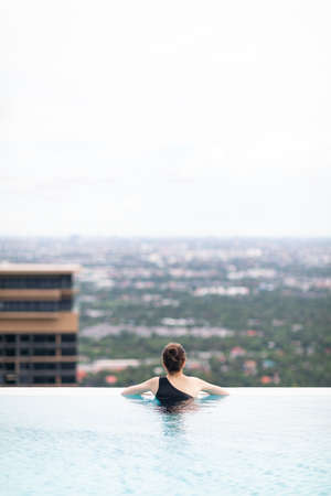 Relaxing at swimming pool on rooftop, Woman enjoying the view with arms raised from swimming poolの写真素材