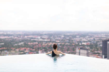 Relaxing at swimming pool on rooftop, Woman enjoying the view with arms raised from swimming poolの写真素材