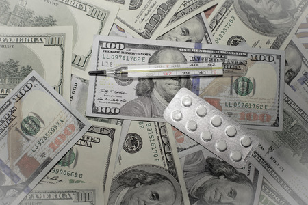 clinical thermometer over dollar banknotes as symbol for high costs in health careの写真素材