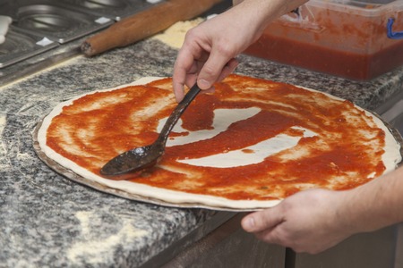 Man chef with raw pizza. Young male in uniform preparing pizza on table.の写真素材