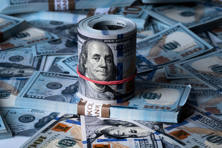 A roll of dollars on the background of scattered one hundred dollar bills