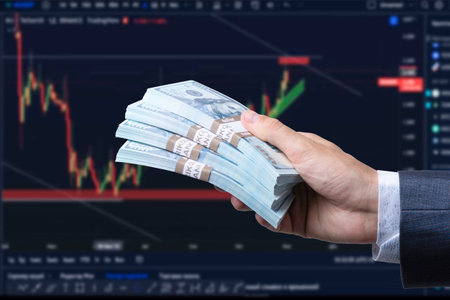 Man's hand holding Dollar (USD) banknotes on stock market background