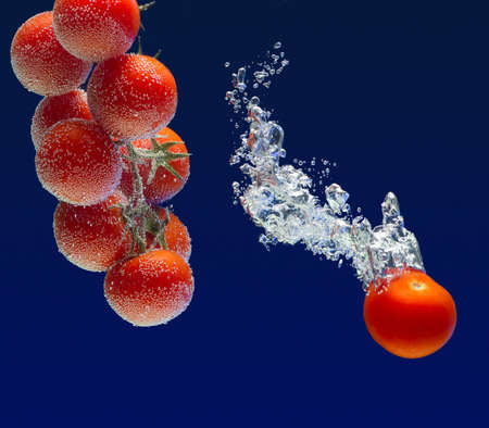 tomatoes in water with splashes on blue backgroundの写真素材