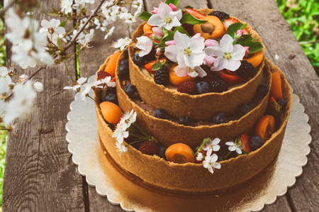 Cheesecake with fruits and berries on the old planks, white apple and cherry flowersの写真素材