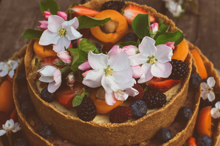 Closeup of the apple and cherry flowers on cheesecake with fruits and berries on the old planksの写真素材