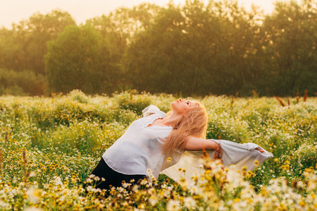 Portrait of young girl dancing in chamomile field under the rain looking to the skyの写真素材
