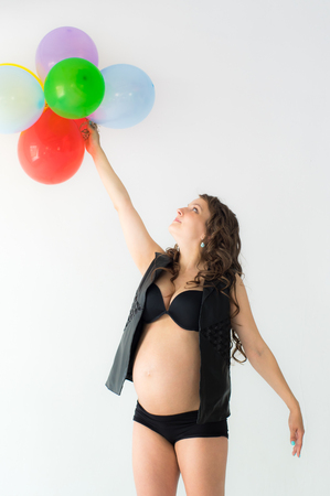 Pregnant woman with balloons and hands above head, white wall on backgroundの写真素材