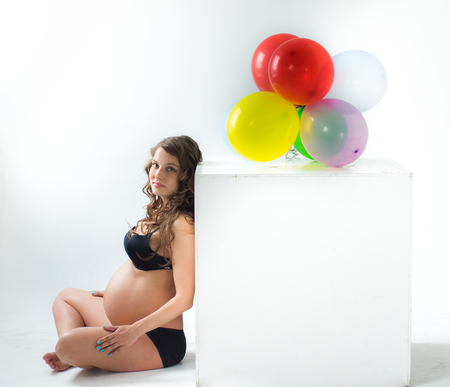 Pregnant woman with balloons sit on floor, white wall on backgroundの写真素材