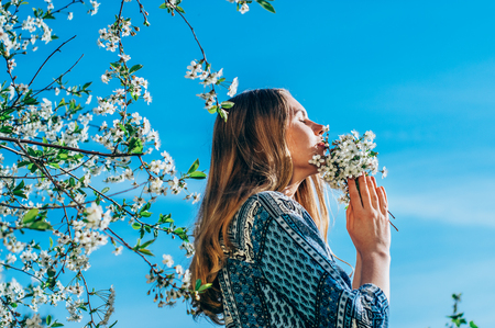 Portrait of young girl in blossom cherry garden, smelling a bouquet of flowers, closed eyesの写真素材