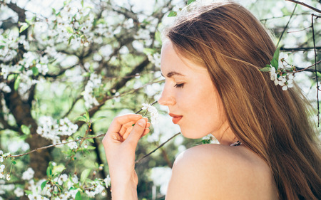 Portrait of young girl in blossom cherry garden, smelling a flower, closed eyesの写真素材