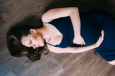 Pregnant woman in dark blue dress lies on the floorの写真素材