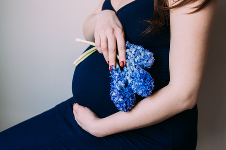 Pregnant woman in dark blue dress sitting with bouquet of flowersの写真素材