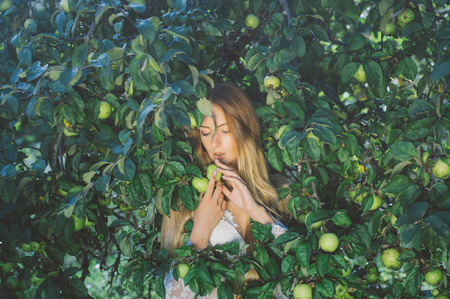 Portrait of young beautiful girl in white lace dress in apple garden, in the crown with apple in handsの写真素材